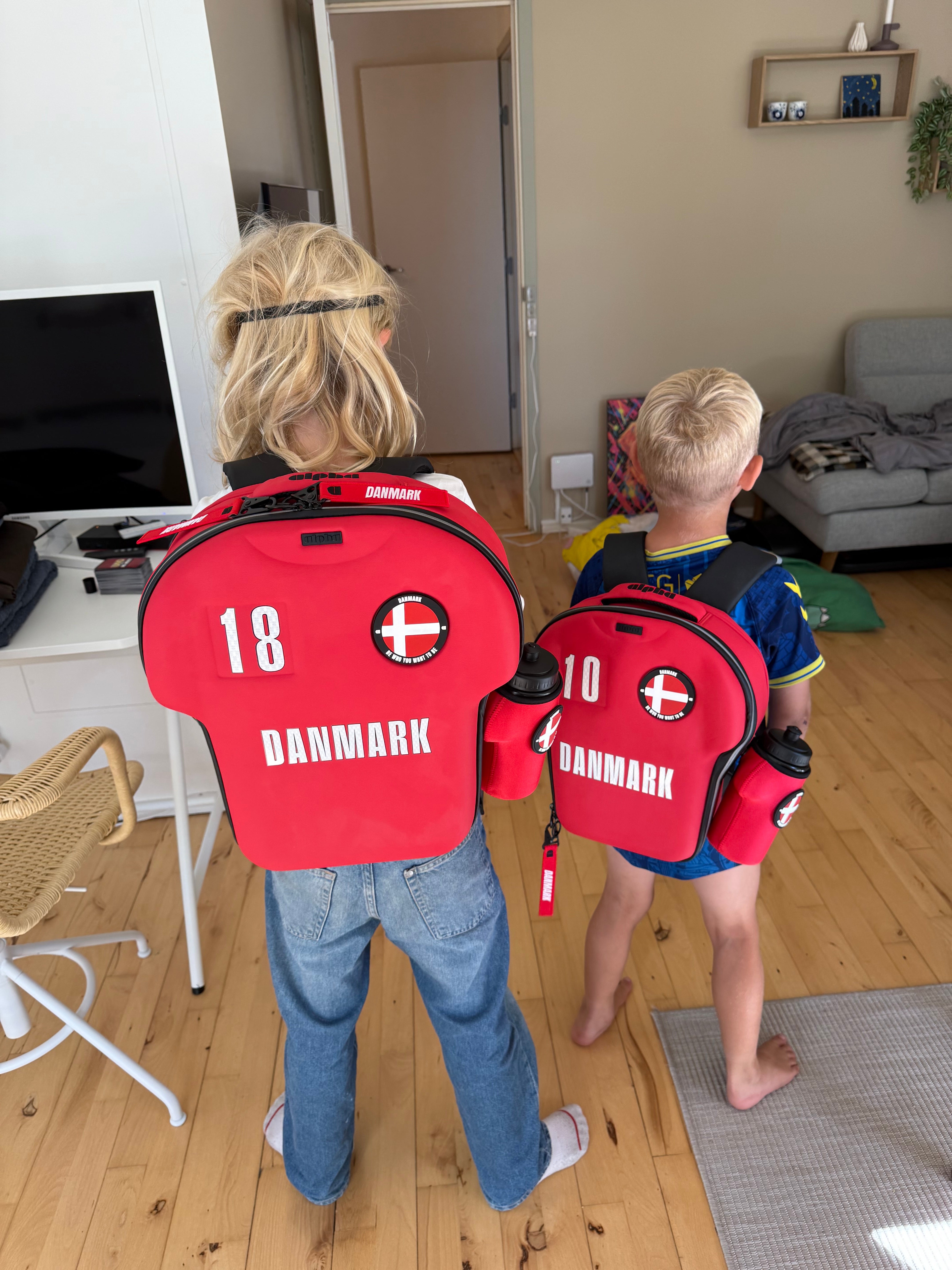 Two children wearing red Shirt Shaped backpacks labeled 'Danmark'