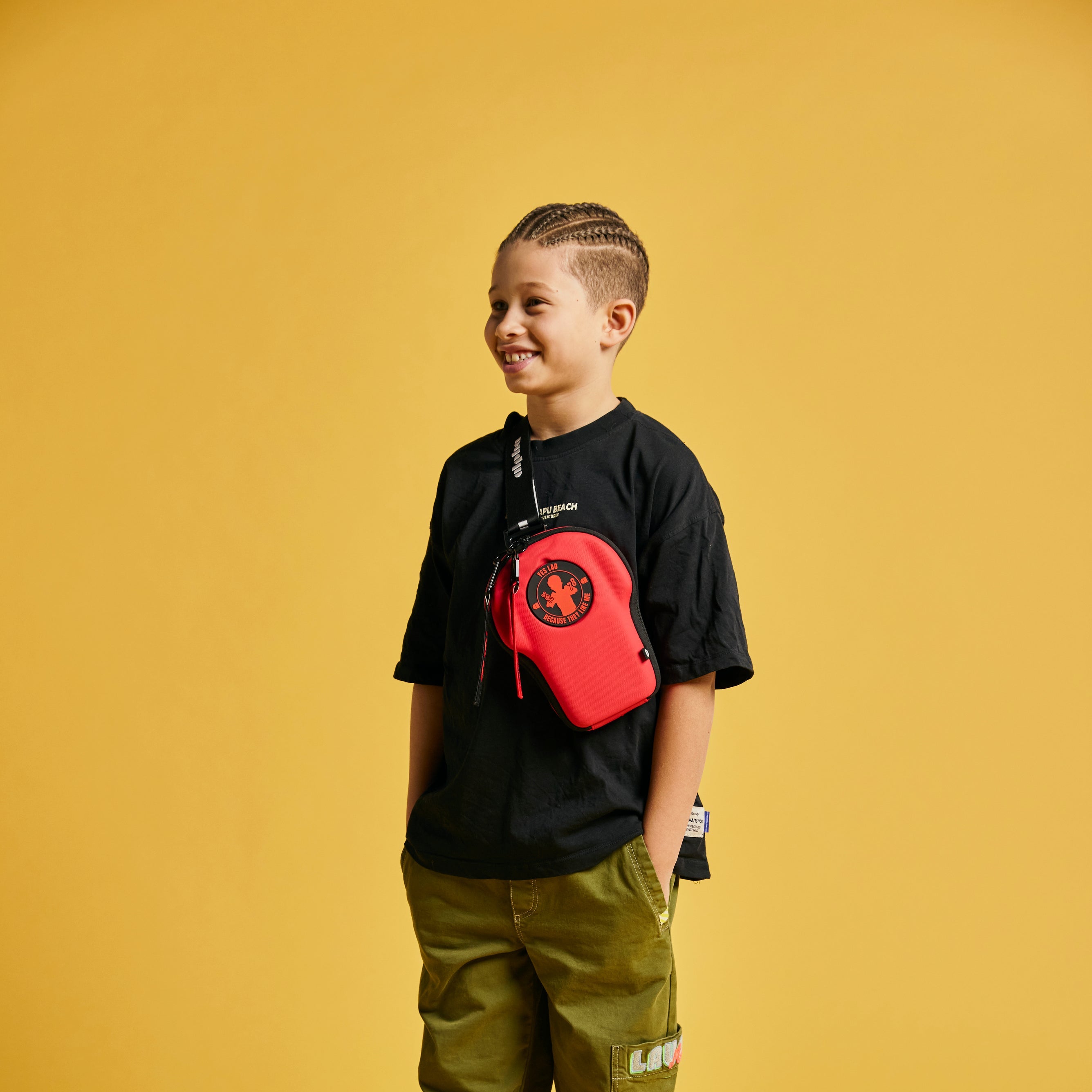 Child wearing a black t-shirt with a red bag, green pants, and blue shoes on a yellow background