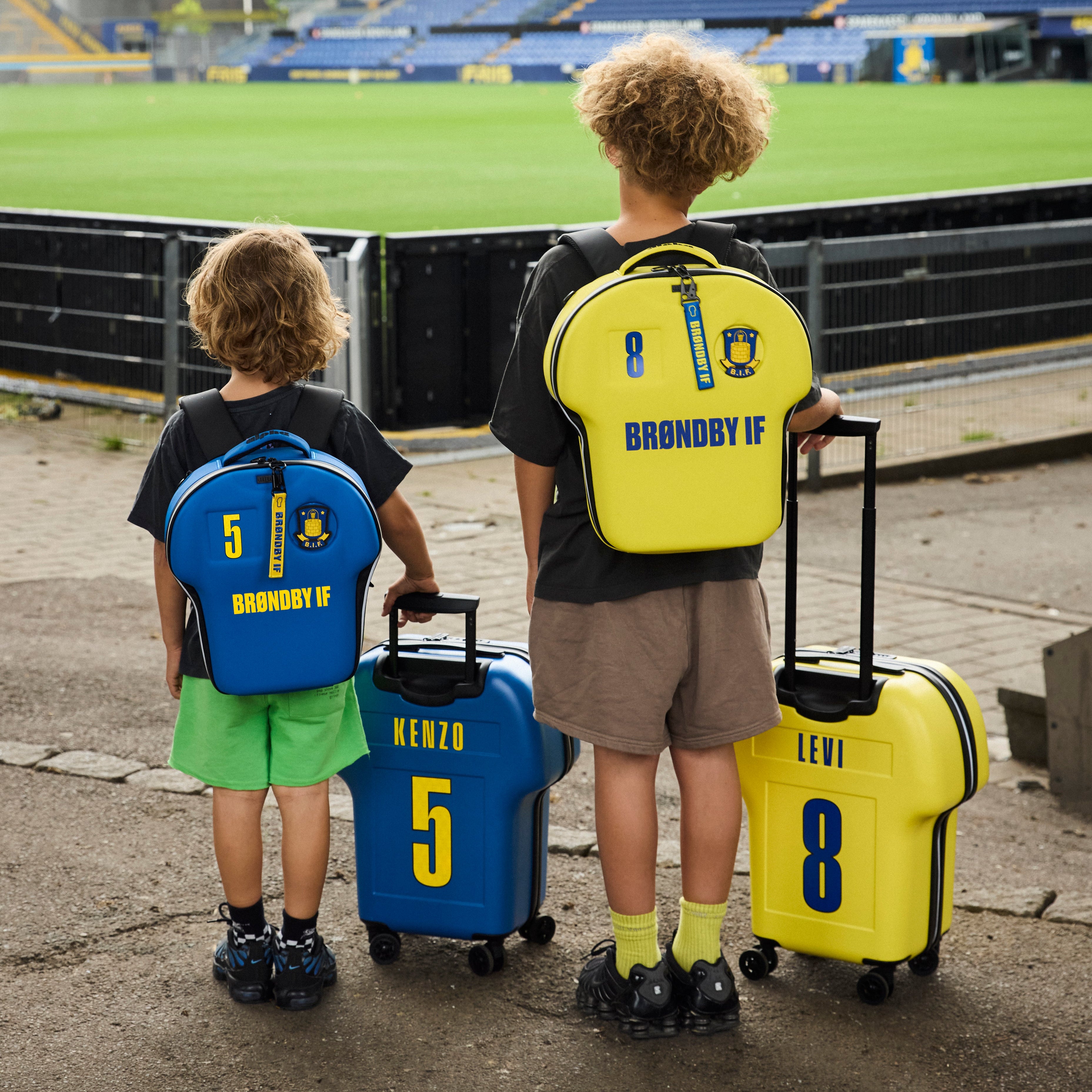 Two children with backpacks and suitcases at a stadium