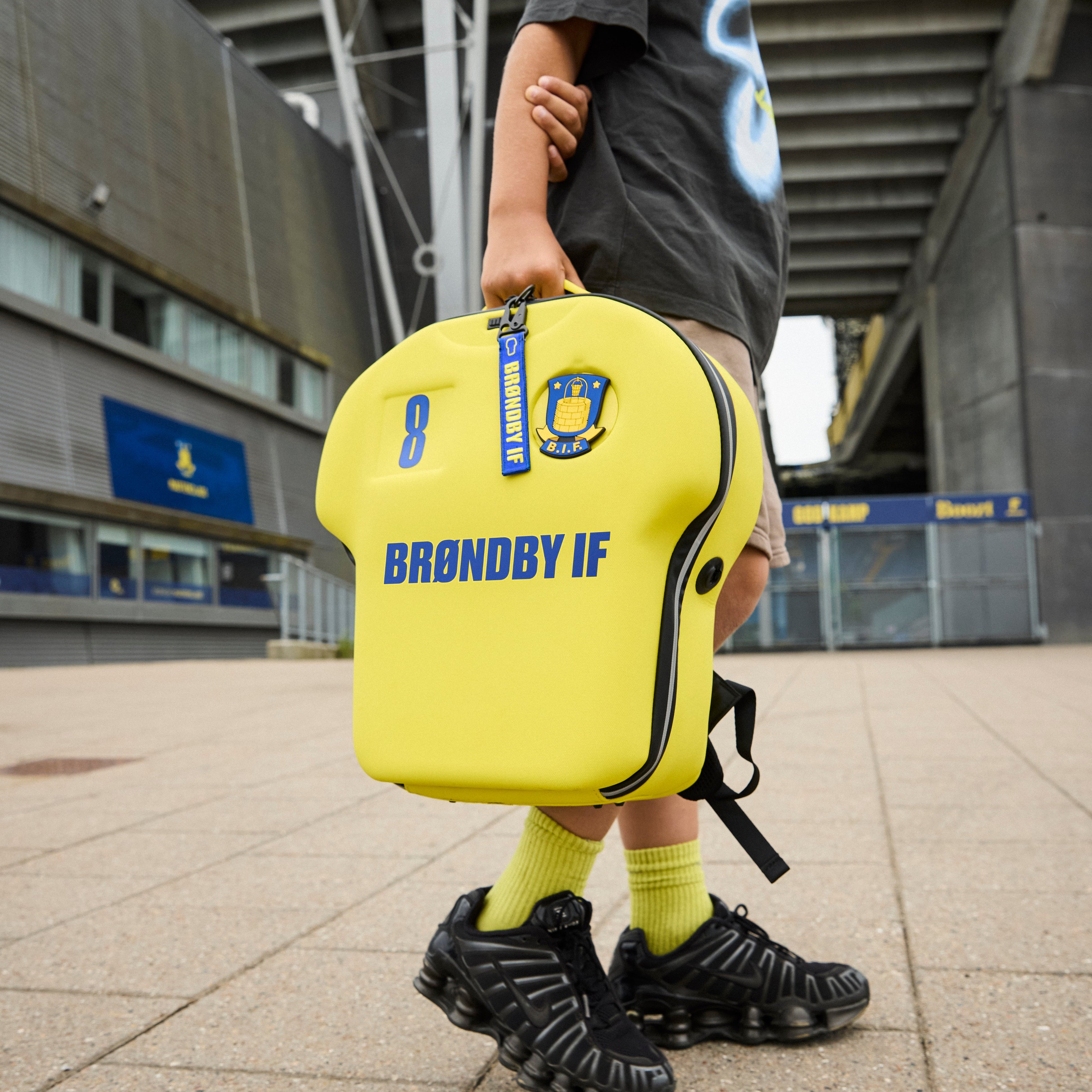 Child holding a yellow sports bag with 'Brøndby IF' branding in an outdoor setting.