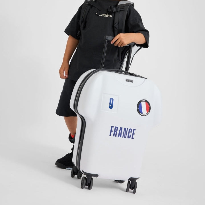 Child holding a white suitcase with 'France' and flag design on a light gray background