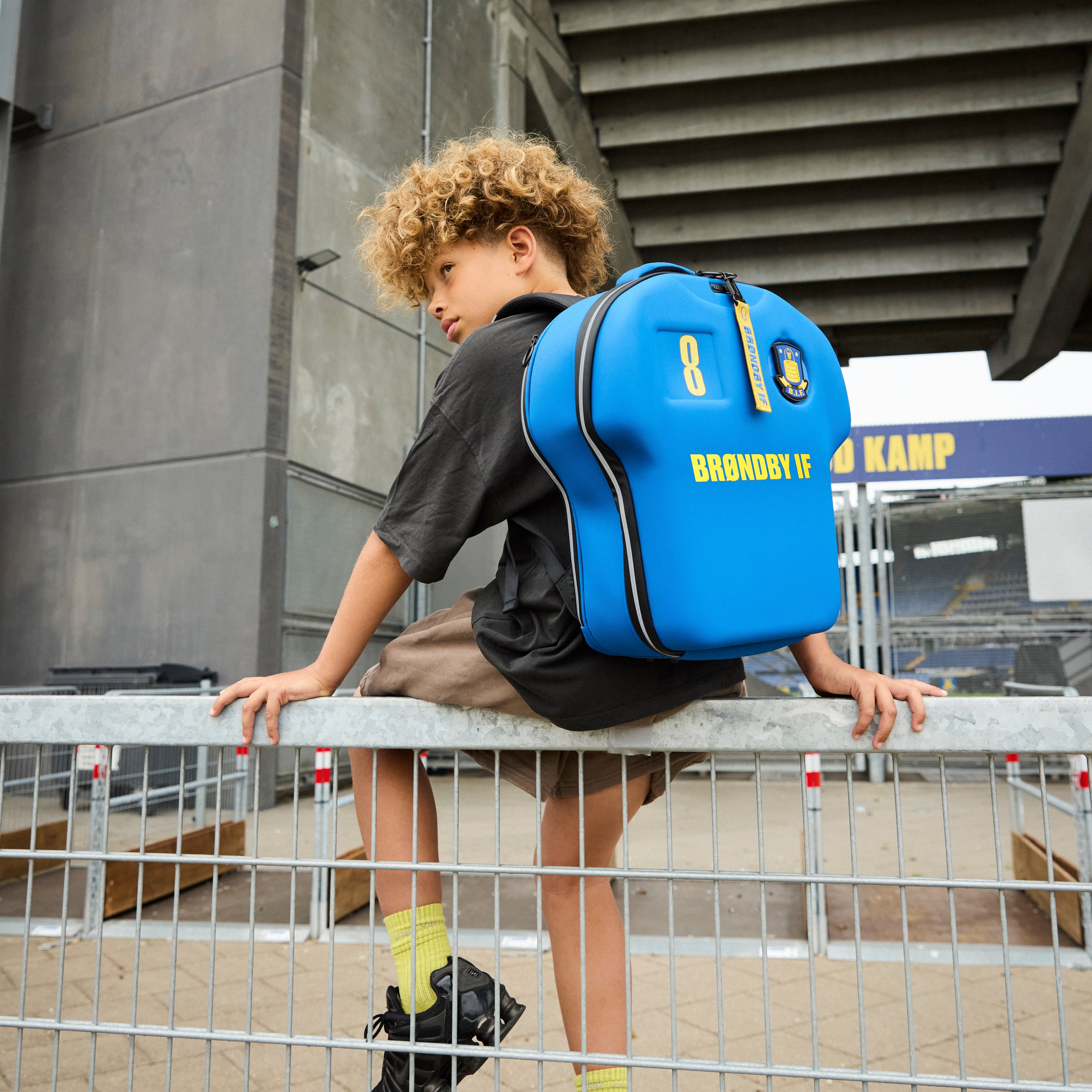 Child with a blue backpack sitting on a railing outside a building.
