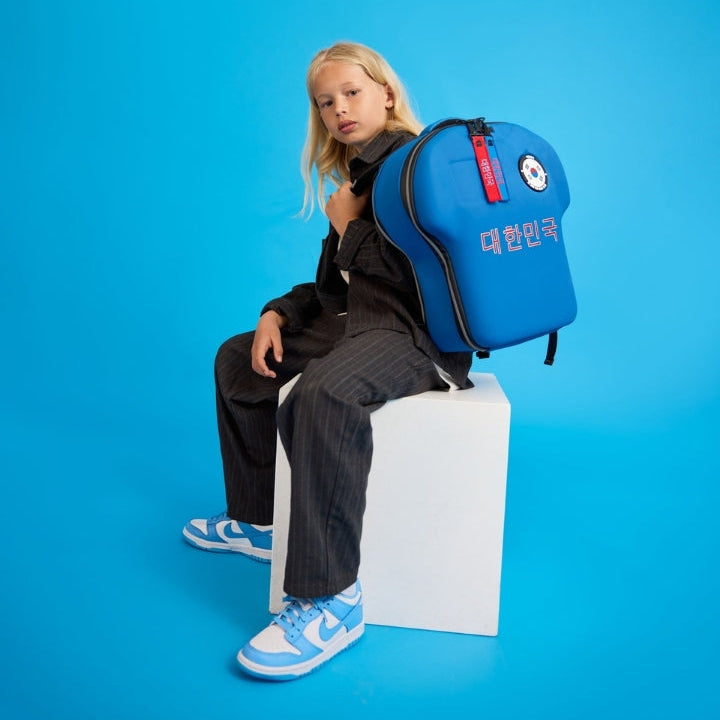 Person sitting on a white block with a blue backpack against a blue background
