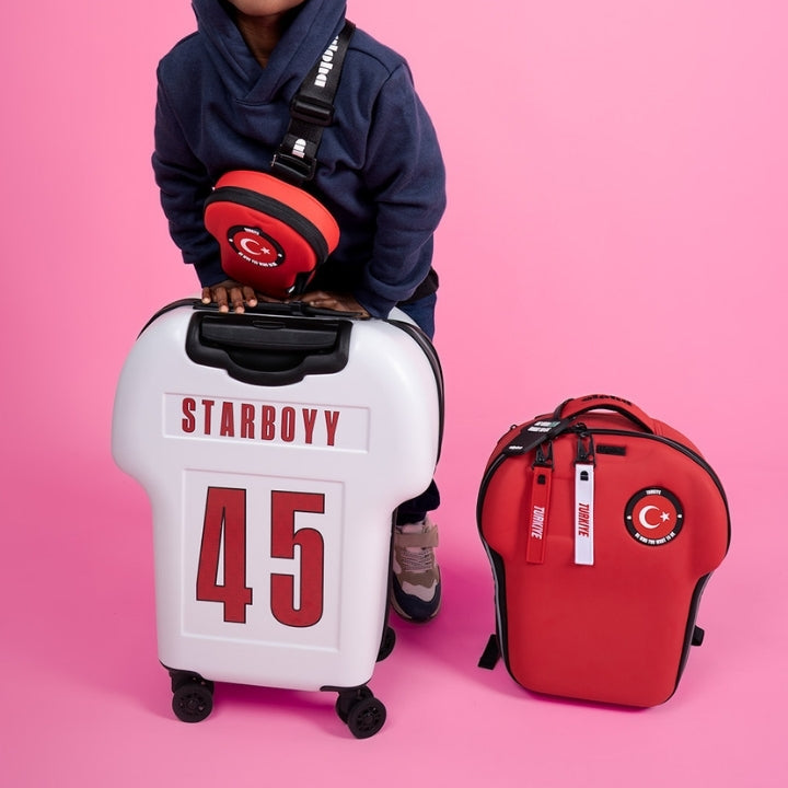 Child with a Starboyv suitcase and red bag on a pink background