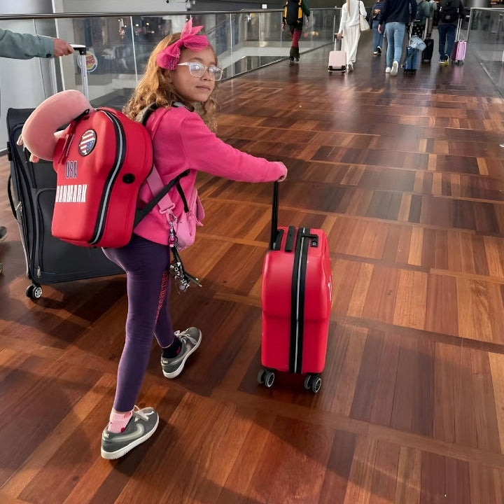 Child with a red suitcase and backpack in an airport terminal