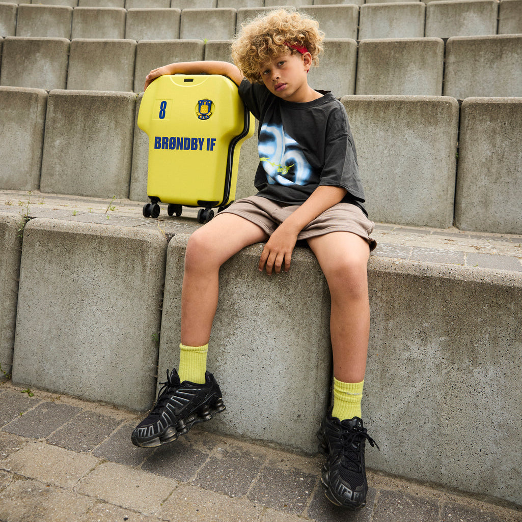 Child sitting on concrete steps with a yellow brøndby IF suitcase