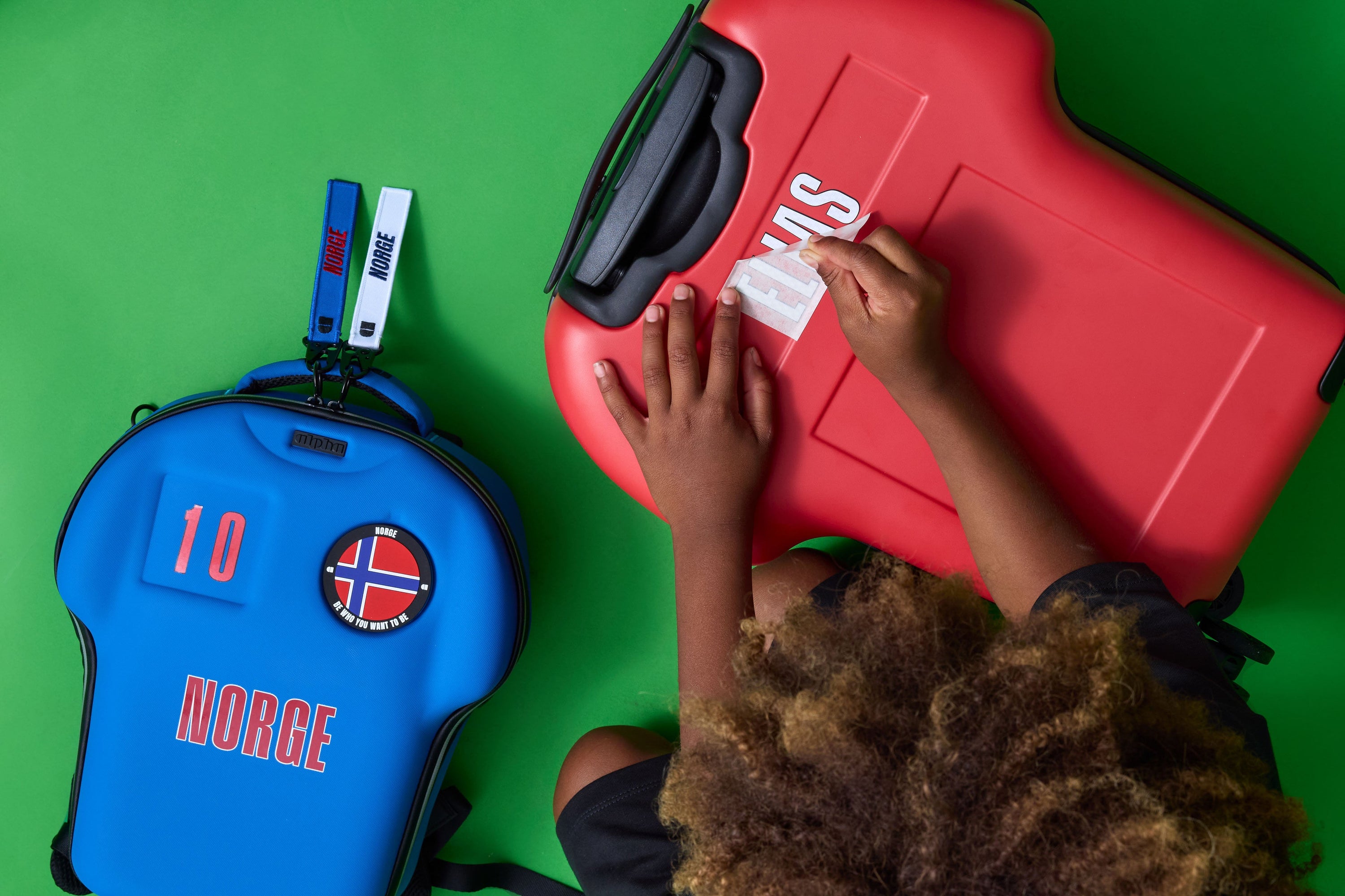 Two suitcases, one red and one blue with a 'Norge' sticker, on a green surface.
