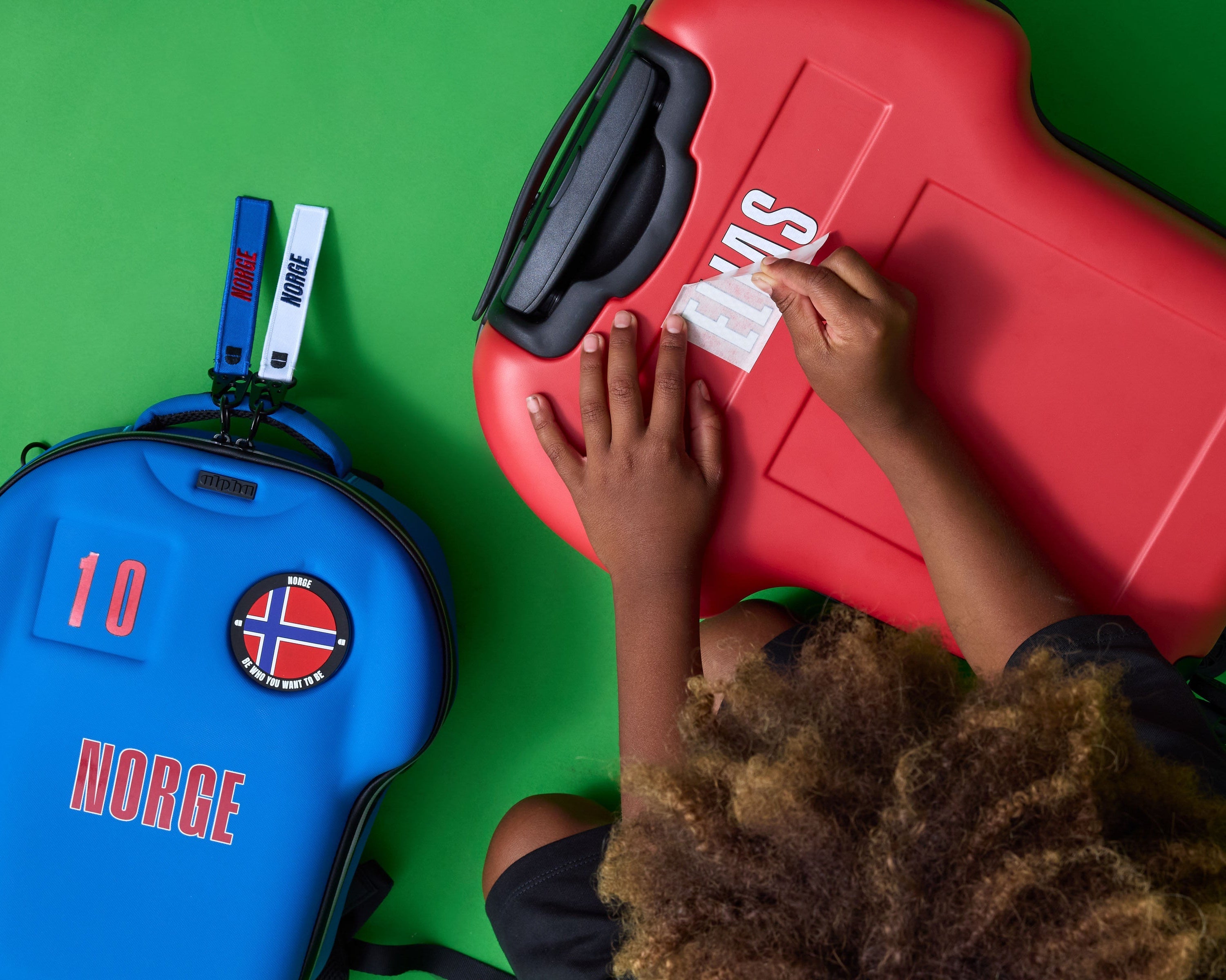 Two suitcases, one red and one blue with a 'Norge' sticker, on a green surface.