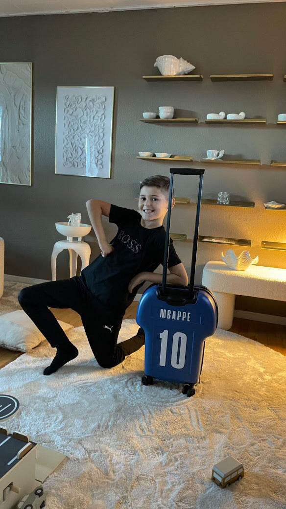 happy kid showing off his shirt-shaped customised cabin luggage with the name MBAPPE on the backside