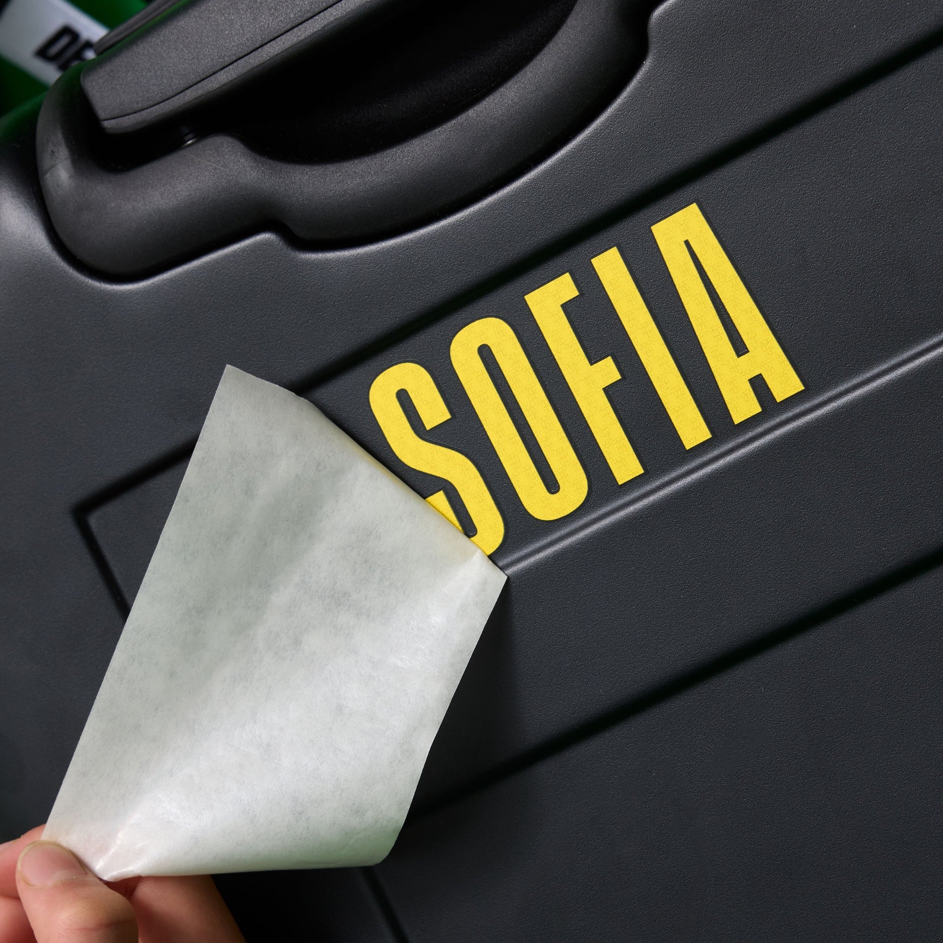 kid applying a yellow 'SOFIA' adhesive stickers to a black cabin luggage by alpha