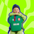 Child wearing a green England jersey with a blue outline against a green wavy background