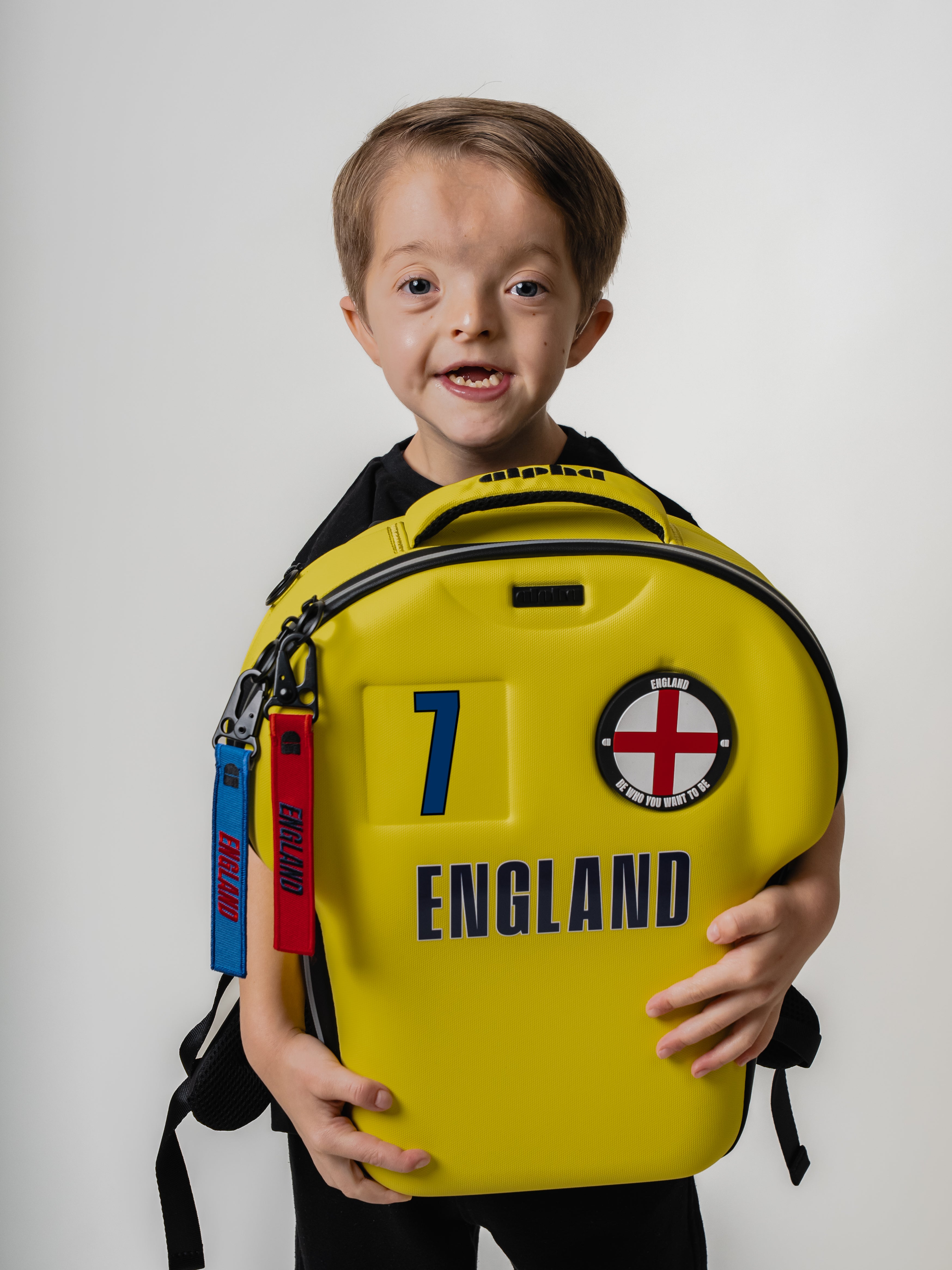 Child holding a yellow backpack with England branding on a white background