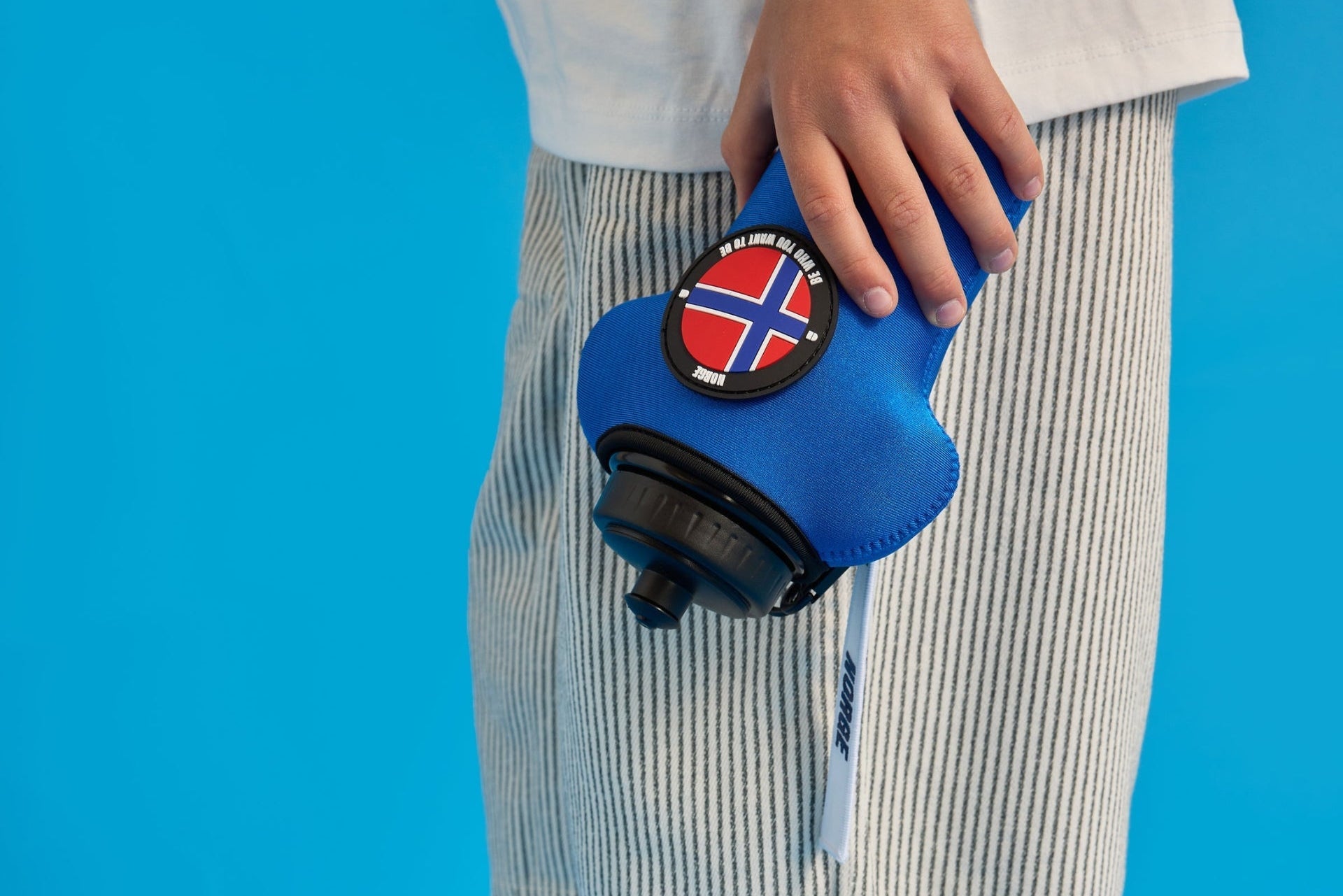 Person holding a blue water bottle with sleeve, with a norge flag design against a blue background